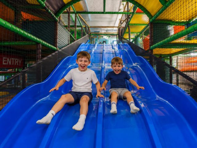 Two children sliding down a fibreglass slide