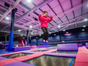 Young girl in a bright pink hoodie and black trousers enjoying an active play experience at an indoor trampoline park.